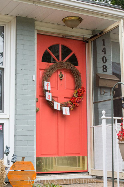 Coral front door on gray painted brick house with fall wreath